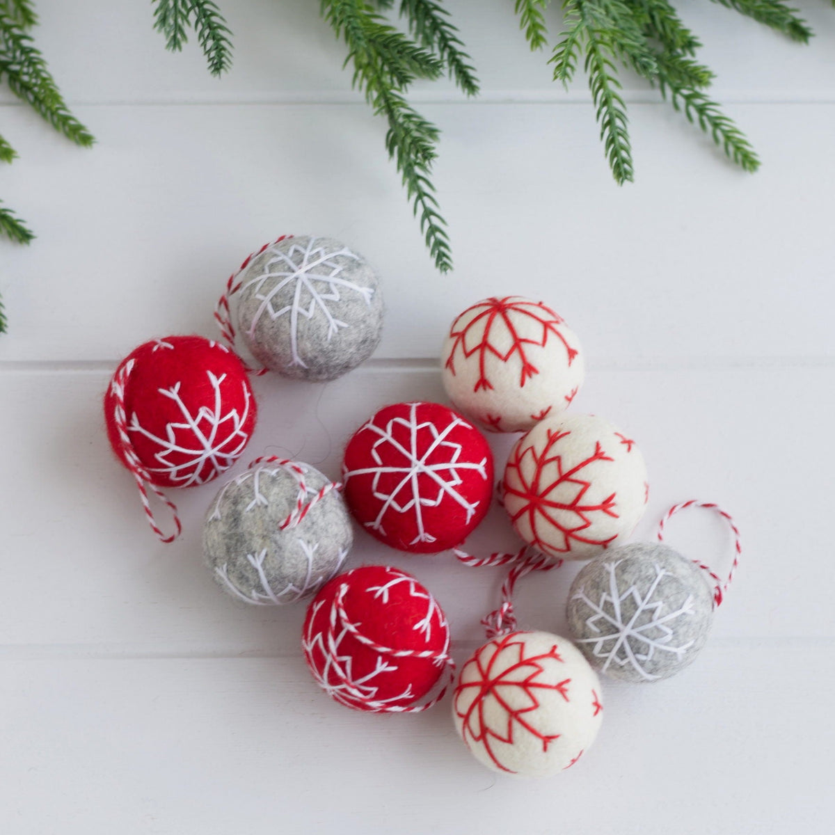 Decorative Christmas balls with red and gray patterns on a white surface with greenery.