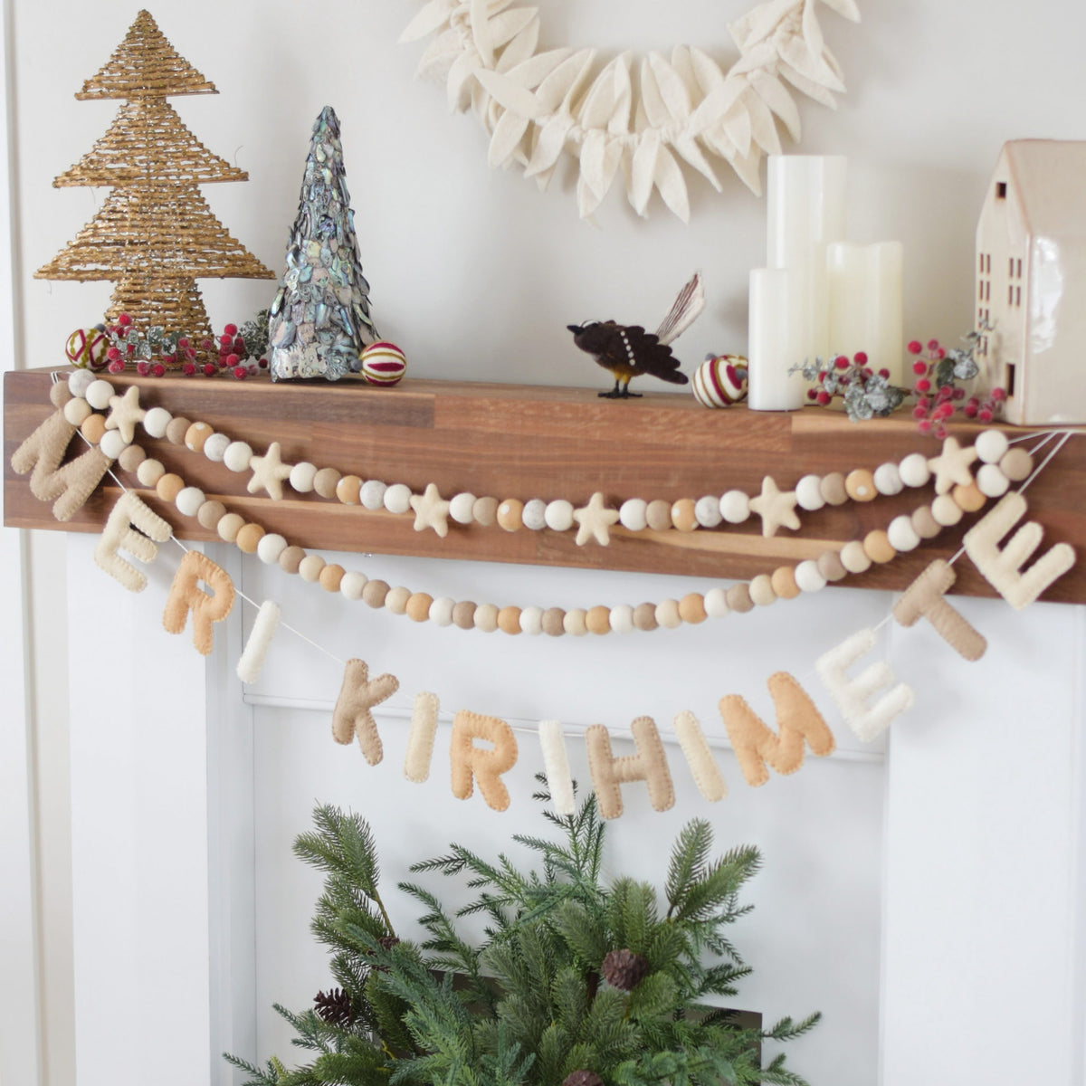 Decorative Christmas mantel with garland, trees, and wreath on a white wall.