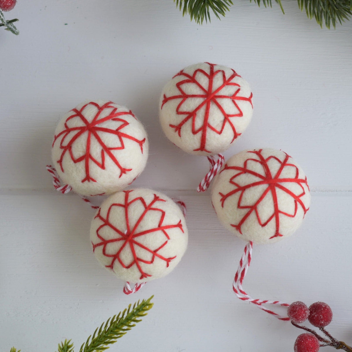 Decorative items with red snowflake patterns on a white surface with greenery and berries.