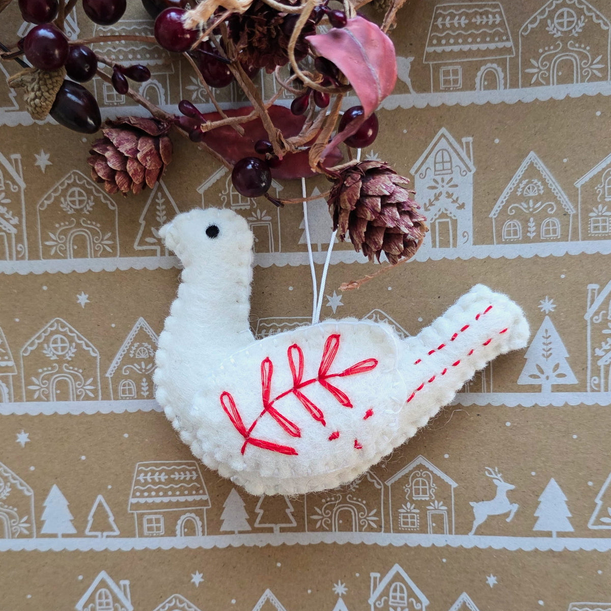 Decorative white bird ornament with red stitching on a patterned background