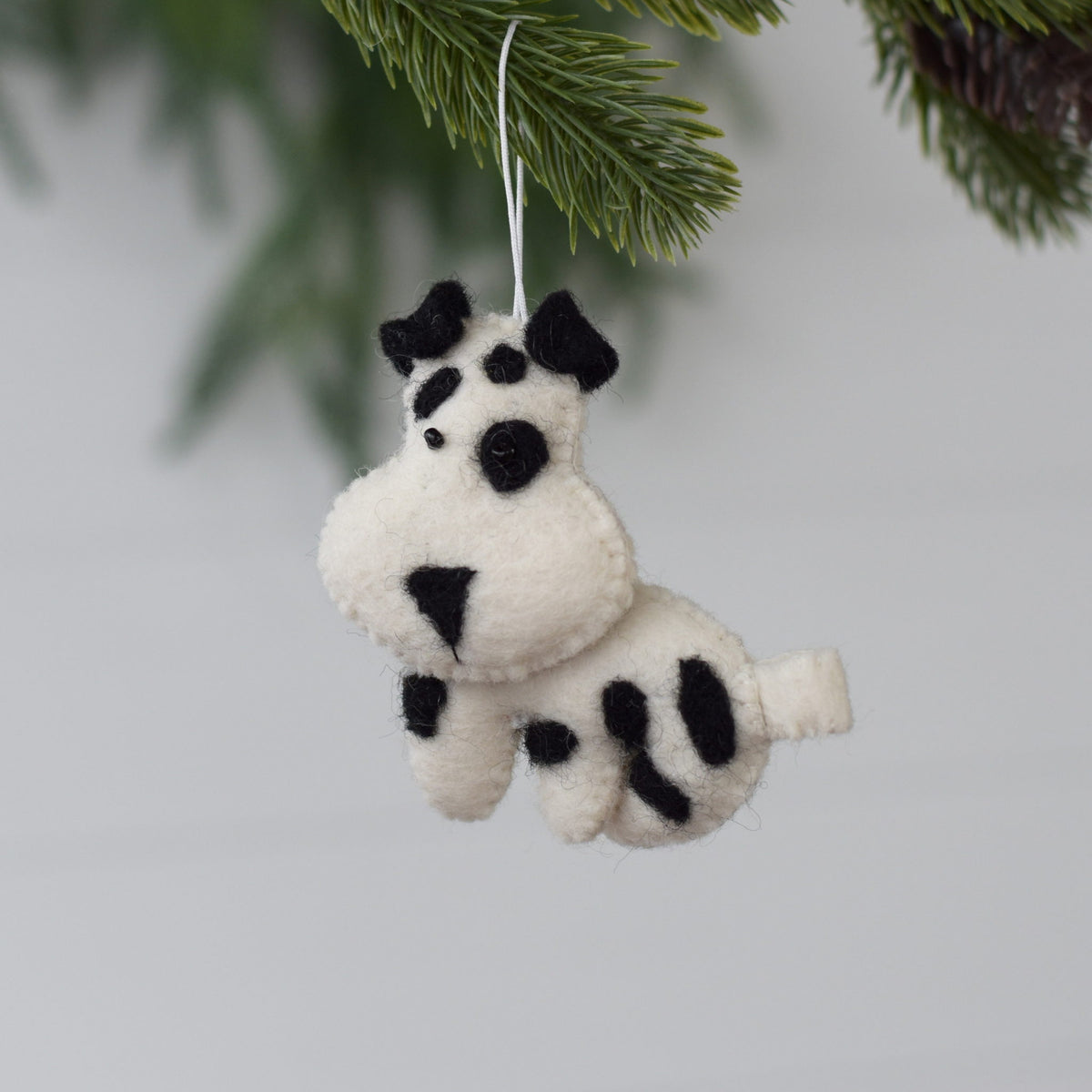 Felted dog ornament hanging from a string with a green pine branch in the background.
